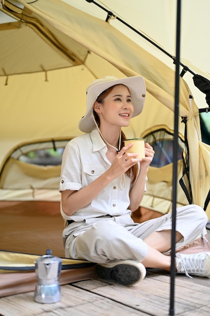 Hübsche asiatische Frau, die einen Kaffee in ihrem Campingzelt schlürft, während sie die schöne Aussicht betrachtet