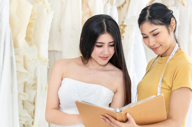 Hübsche asiatische Frau, die Kleid in einem Geschäft mit Schneiderassistent wählt.