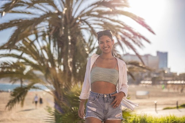 Hübsche asiatische Frau im Sommer neben einer Palme am Strand bei Sonnenuntergang