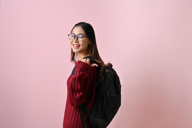 Hübsche asiatische Studentin steht mit ihrem Rucksack vor einem isolierten rosa Hintergrund