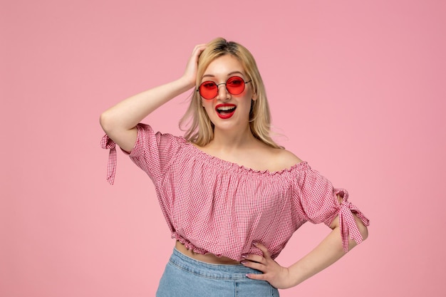 Hübsche blonde Dame des netten Mädchens, die rote Brille im rosa Hemd trägt, das Kopf mit dem großen Lächeln hält