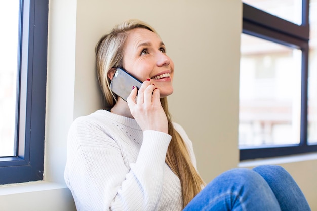 Hübsche blonde Frau des jungen Erwachsenen, die zu Hause ihr Smartphone verwendet