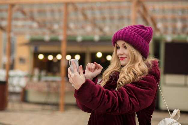 Hübsche blonde Frau, die eine Nachricht auf einem Handy eintippt