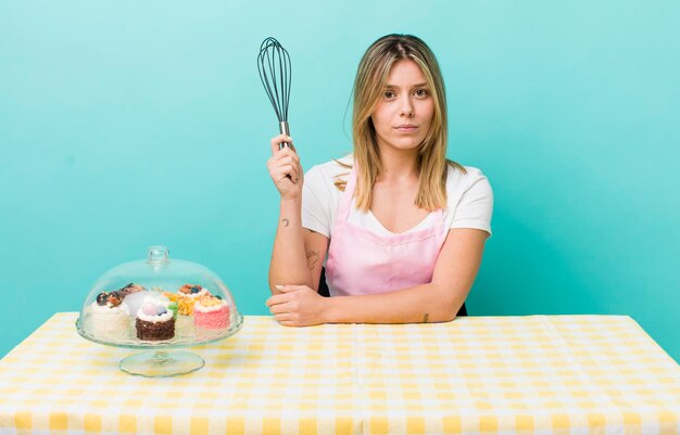 Hübsche blonde Frau, die sich traurig, verärgert oder wütend fühlt und auf das Konzept des hausgemachten Kuchens blickt