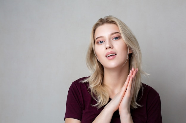 Hübsche blonde Frau im roten T-Shirt, das über einem grauen Hintergrund aufwirft. Platz für Text