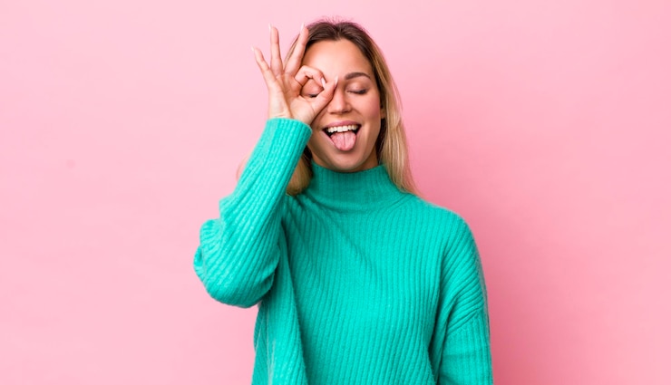 Foto hübsche blonde frau lächelt glücklich mit lustigem gesicht, scherzt und schaut durch das guckloch, um geheimnisse auszuspionieren