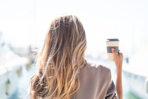 Hübsche blonde Uruguayerin hält im Freien in Rückenposition einen Kaffee zum Mitnehmen
