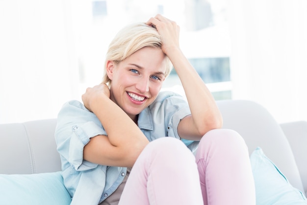 Hübsche Blondine, die auf der Couch sitzen und an der Kamera lächeln