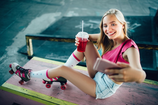 Hübsche Blondine, die auf rosa Boden sitzen und selfie nehmen