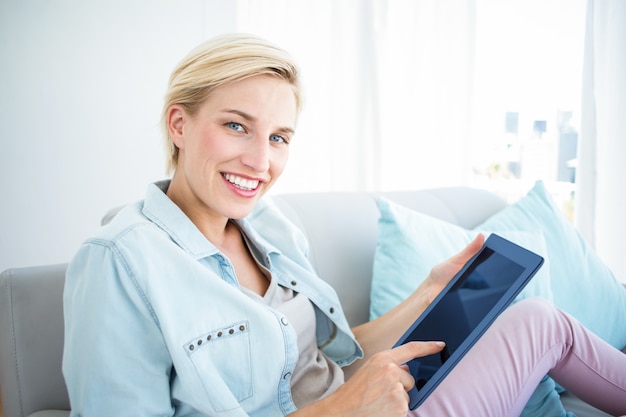 Hübsche Blondine, die ihre Tablette auf der Couch verwenden