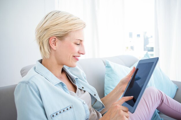 Hübsche Blondine, die ihre Tablette auf der Couch verwenden