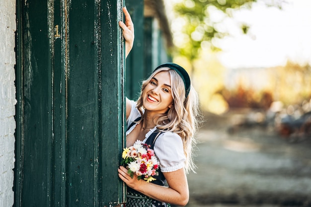 Hübsche Blondine im Dirndl, traditionelles Oktoberfestkleid, das auf der Farm nahe Holztür steht