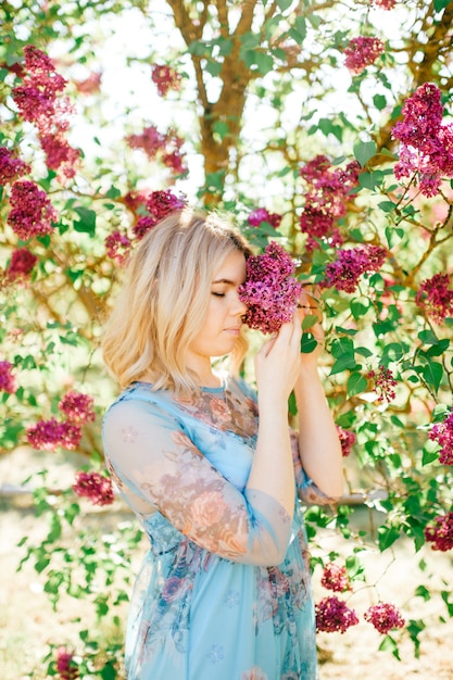 Hübsche Blondine im schönen blauen Kleid, das in blühenden Büschen aufwirft.