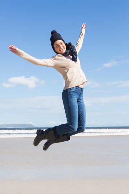 Hübsche Blondine in den Jeans, die auf den Strand springen