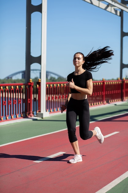 Hübsche brünette Frau, die bei Tageslicht auf der Joggingstrecke läuft