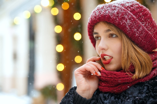 Hübsche brünette Frau mit Strickmütze und Schal, die auf dem Bokeh-Hintergrund posiert. Freiraum