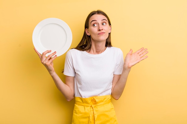 Hübsche Cheffrau des jungen Erwachsenen, die eine leere Platte hält