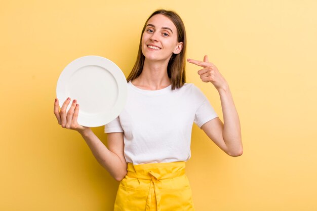 Hübsche Cheffrau des jungen Erwachsenen, die eine leere Platte hält