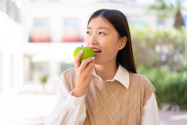 Hübsche Chinesin an draußen, die einen Apfel hält