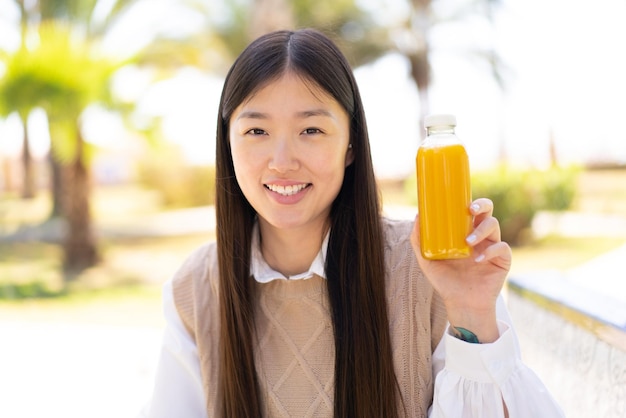 Hübsche Chinesin, die draußen einen Orangensaft hält und viel lächelt