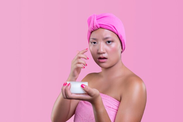 Hübsche Chinesin, die sich um ihre Haut kümmert, isoliert vom rosa Hintergrund, Schönheitskonzept