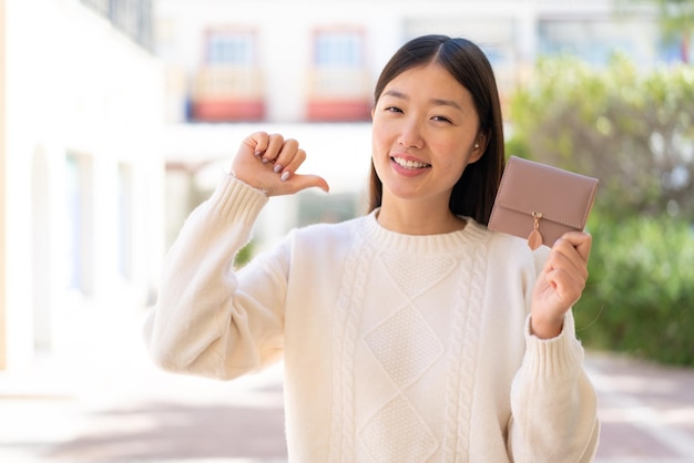 Hübsche Chinesin hält stolz und selbstzufrieden eine Brieftasche im Freien