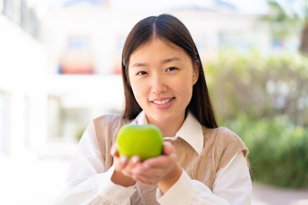 Hübsche Chinesin im Freien, die einen Apfel mit glücklichem Ausdruck hält
