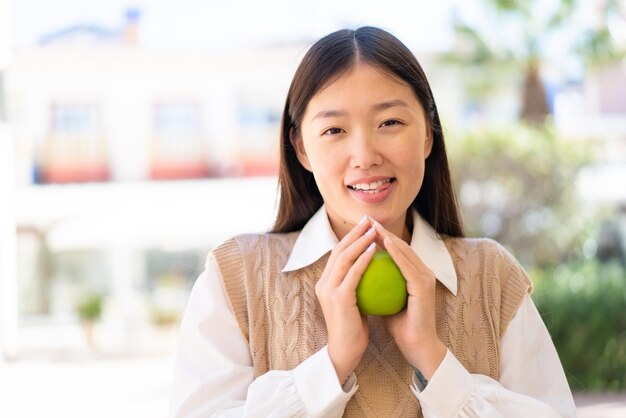 Hübsche Chinesin im Freien, die einen Apfel mit glücklichem Ausdruck hält