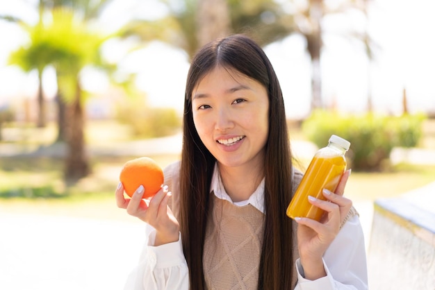 Hübsche Chinesin im Freien mit einer Orange und einem Orangensaft