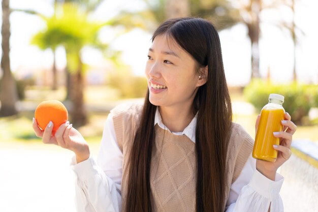 Hübsche Chinesin im Freien mit einer Orange und einem Orangensaft