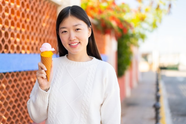 Hübsche Chinesin mit Cornet-Eis im Freien, die viel lächelt