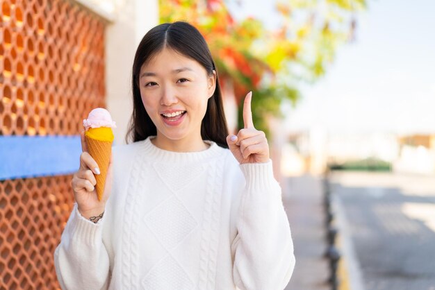 Hübsche Chinesin mit einem Cornet-Eis im Freien und zeigt eine tolle Idee