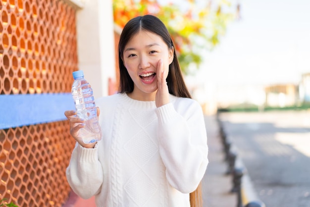 Hübsche Chinesin mit einer Flasche Wasser im Freien, die mit weit geöffnetem Mund schreit