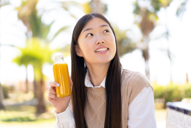 Hübsche chinesische Frau, die draußen einen Orangensaft hält und dabei lächelt