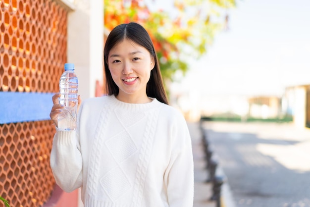 Hübsche chinesische Frau mit einer Flasche Wasser im Freien, die viel lächelt