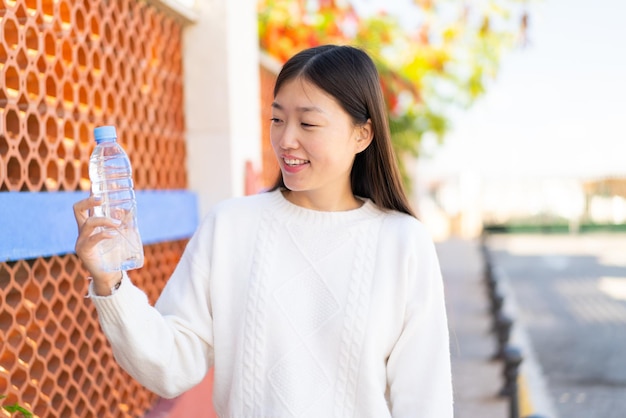 Hübsche chinesische Frau mit einer Flasche Wasser im Freien mit glücklichem Gesichtsausdruck