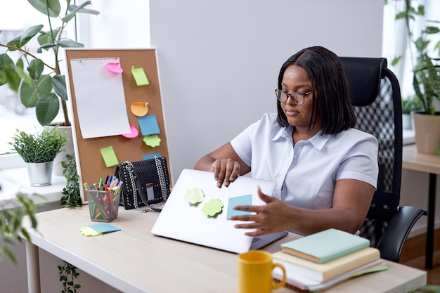 Hübsche Dame, die den Laptop öffnet, der morgens im Büro, allein, am Arbeitsplatz zur Arbeit geht. attraktive frau in weißem formellem hemd, das sich auf die arbeit, geschäftsideen und pläne vorbereitet. Online-Arbeit, Job, Beruf