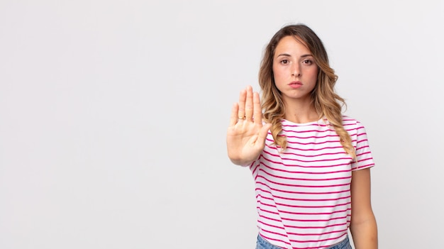 Hübsche dünne Frau, die ernst, streng, unzufrieden und wütend aussieht und eine offene Handfläche zeigt, die eine Stopp-Geste macht