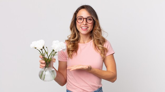 Hübsche dünne Frau, die fröhlich lächelt, sich glücklich fühlt und ein Konzept zeigt und dekorative Blumen hält