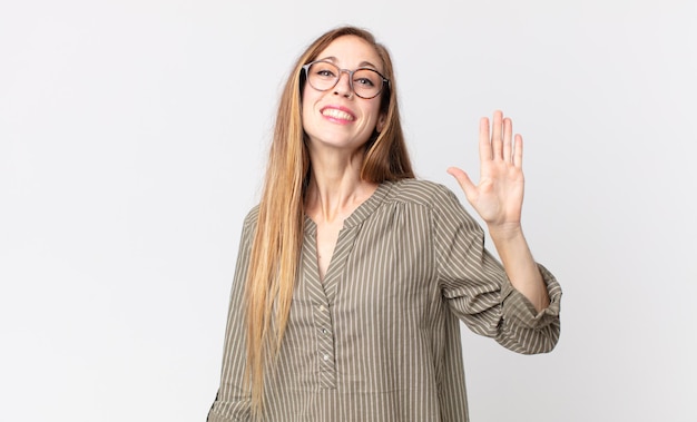 Foto hübsche dünne frau, die glücklich und fröhlich lächelt, die hand winkt, sie begrüßt und begrüßt oder sich verabschiedet