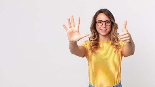 Hübsche dünne Frau, die lächelt und freundlich aussieht, die Nummer sechs oder sechs mit der Hand nach vorne zeigt und herunterzählt