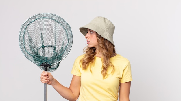 Hübsche dünne Frau in der Profilansicht, die nachdenkt, sich vorstellt oder träumt, einen Hut trägt und ein Fischnetz hält