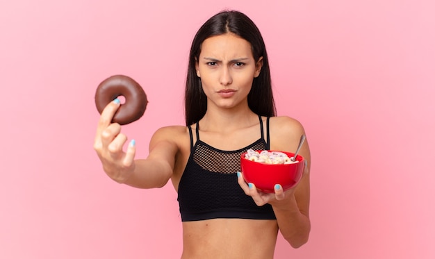 Hübsche Fitnessfrau mit Donut und Frühstücksschüssel