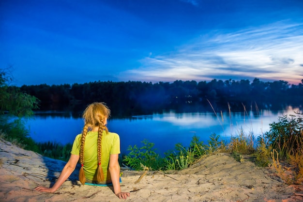 Hübsche Frau am Strand mit Blick auf den Sonnenuntergang über dem Fluss mit blauem Nachthimmel mit Sternen