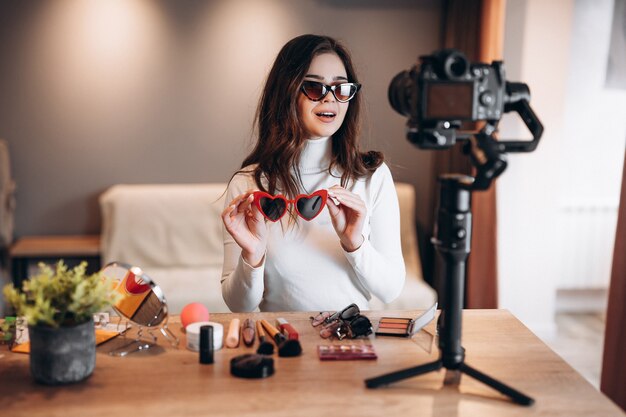 Hübsche Frau der Schönheitsbloggerin in der Sonnenbrille, die das tägliche Make-up-Routine-Tutorial vor der Kamera filmt.