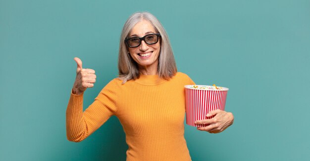 Hübsche Frau des grauen Haares mit einem Popcorn-Eimer