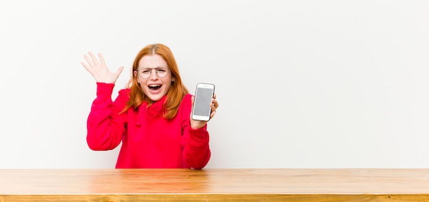 Hübsche Frau des jungen roten Kopfes vor einem Holztisch mit einem Handy