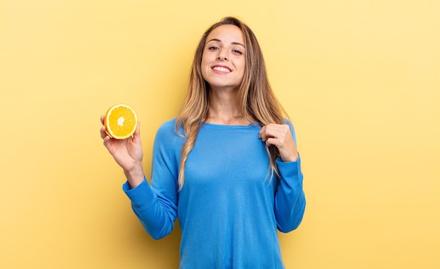 Hübsche Frau, die arrogant, erfolgreich, positiv und stolz aussieht und eine halbe Orange hält