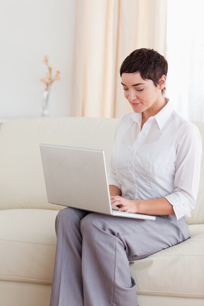 Hübsche Frau, die auf einem Sofa mit einem Laptop sitzt