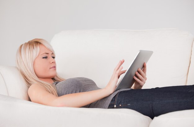 Hübsche Frau, die auf einem Sofa sich entspannt auf einer Linie von Tablet-Computern liegt